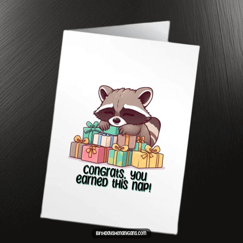 Funny Free Printable Congratulations Card: A sleepy raccoon finding the ultimate comfort on a pile of congratulatory presents.