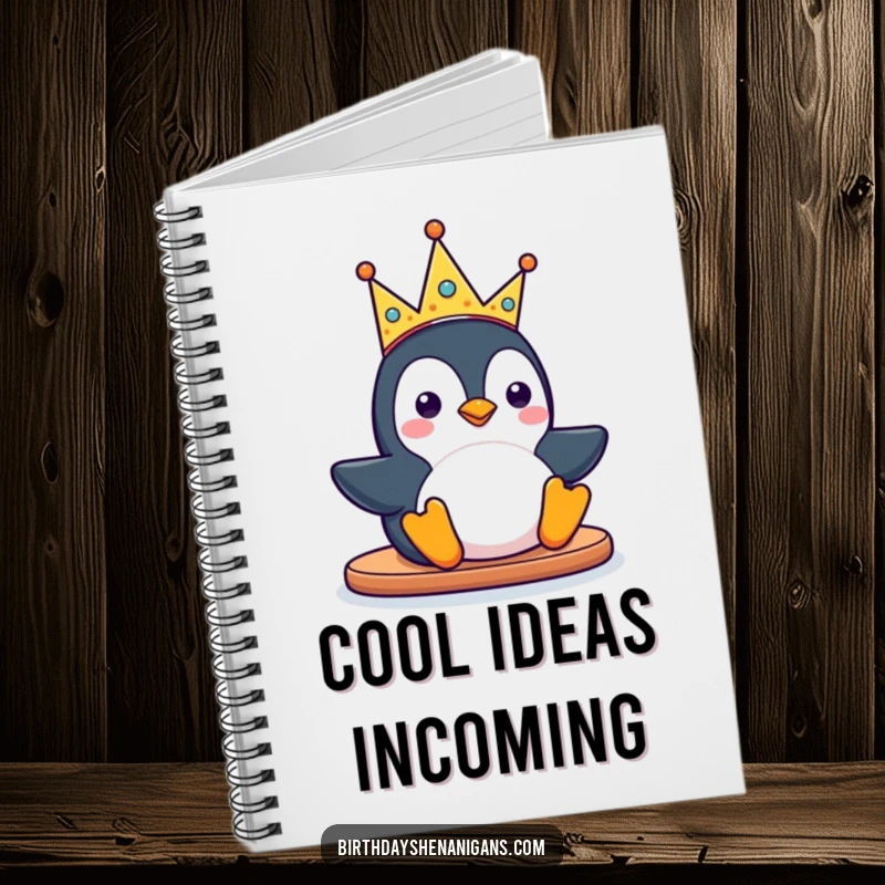 Funny kawaii penguin character sliding with a silly party crown on a notebook, inspiring creativity and organization with its playful design.