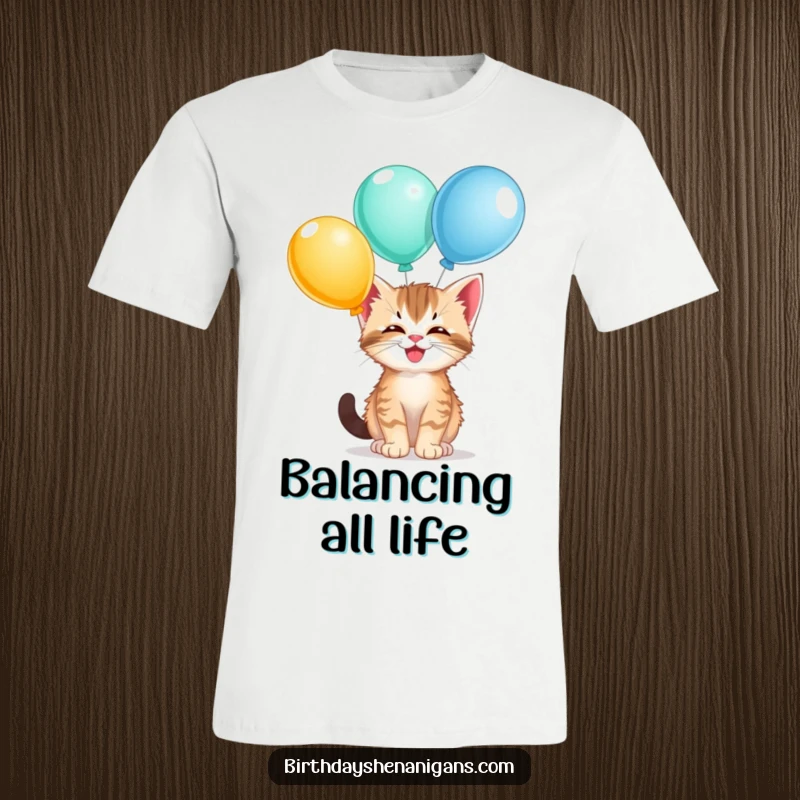 Funny kitten t-shirt, giggling, balancing balloons on nose, playful, cute cat, celebration attire, humorous.