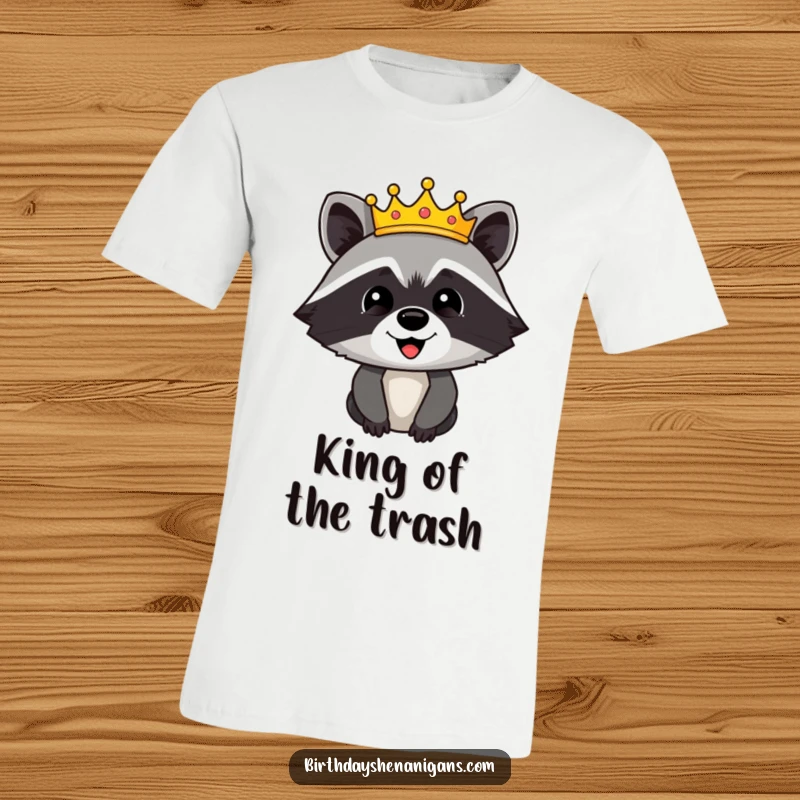 Funny t-shirt featuring a happy raccoon character sporting a grand, festive crown, looking quite pleased with its royal status.